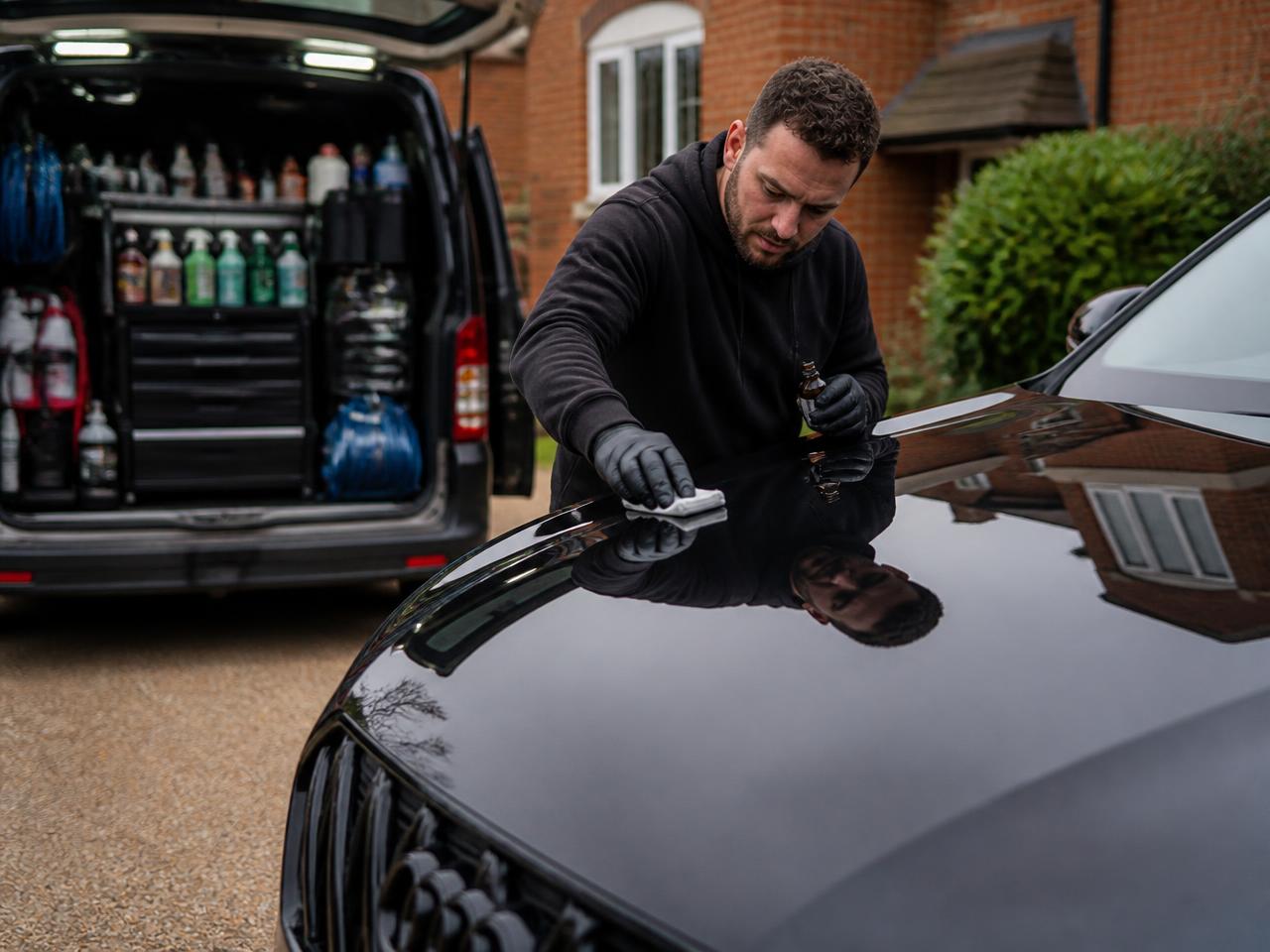 Mobile detailer applying ceramic coating to a black SUV on a driveway
